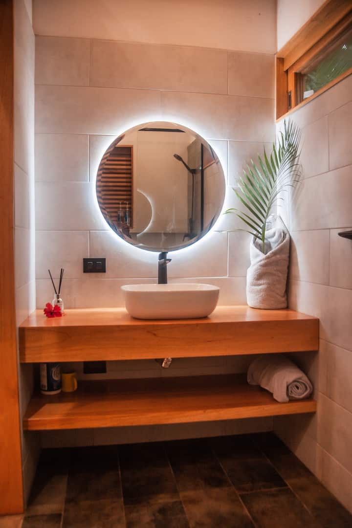 Lavamanos sobre mueble de madera con espejo redondo iluminado