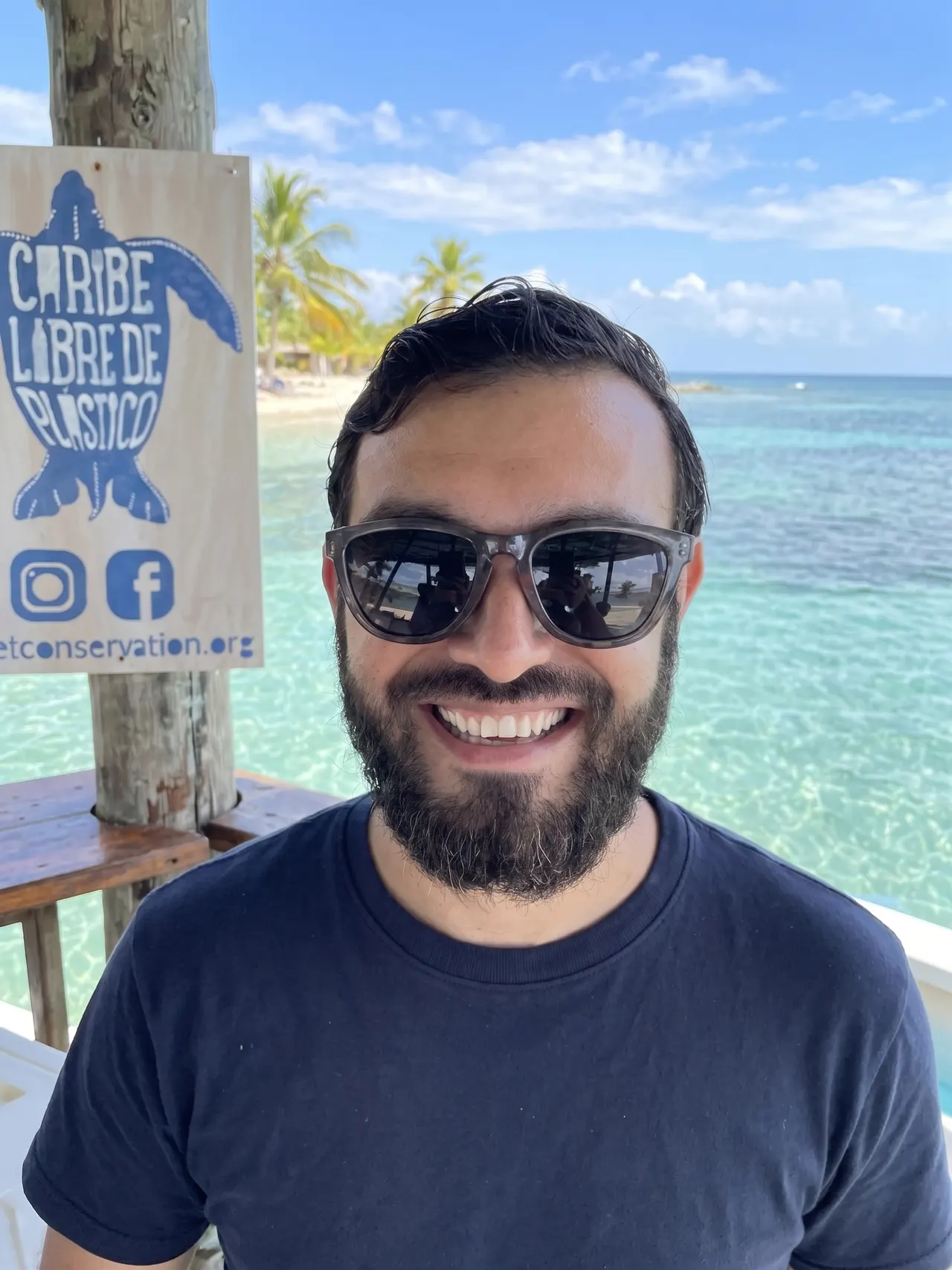 Un hombre sonríe con las gafas puestas, frente al mar