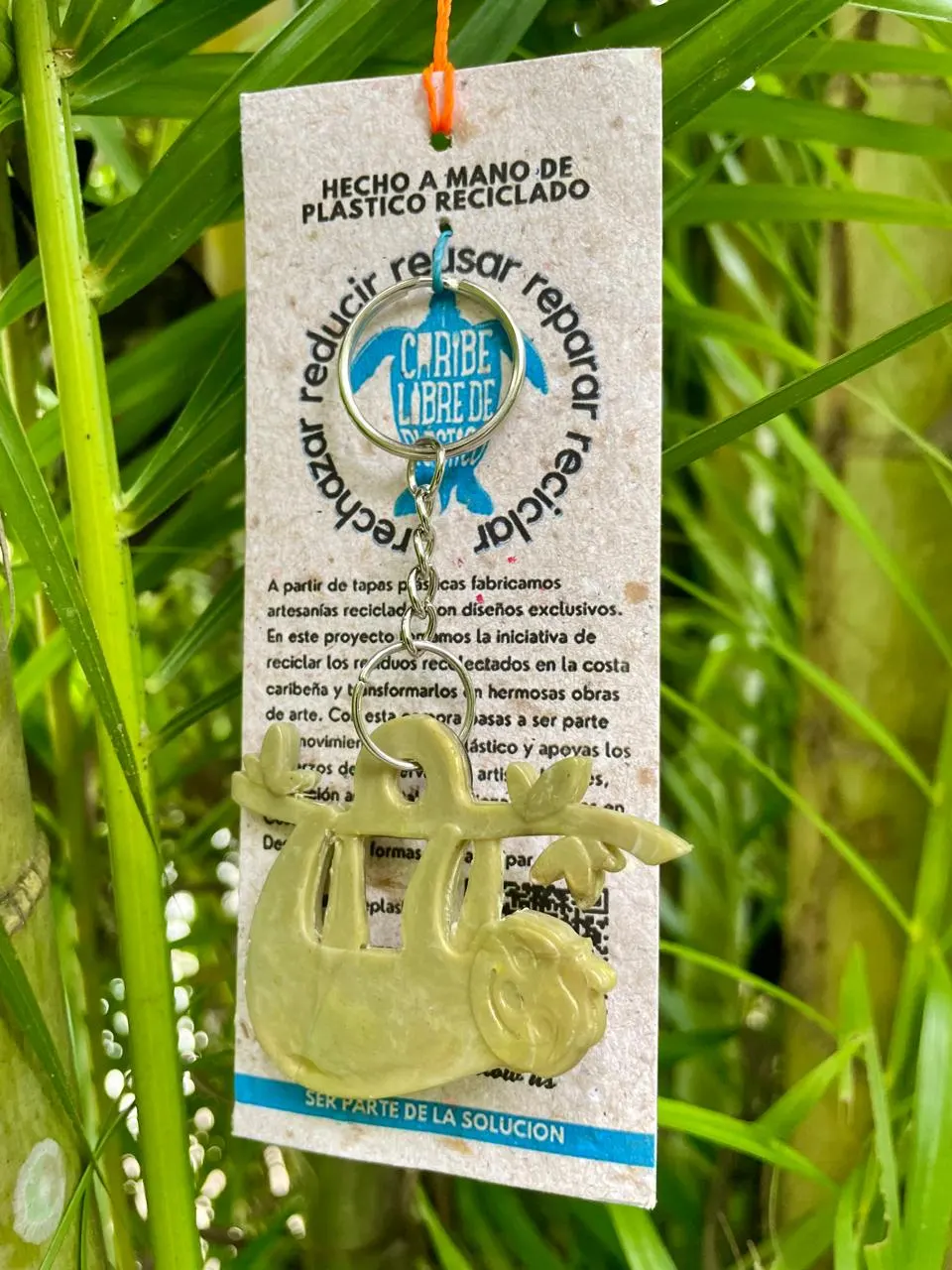 Llavero verde con forma de perezoso sobre su tarjeta de plástico reciclado