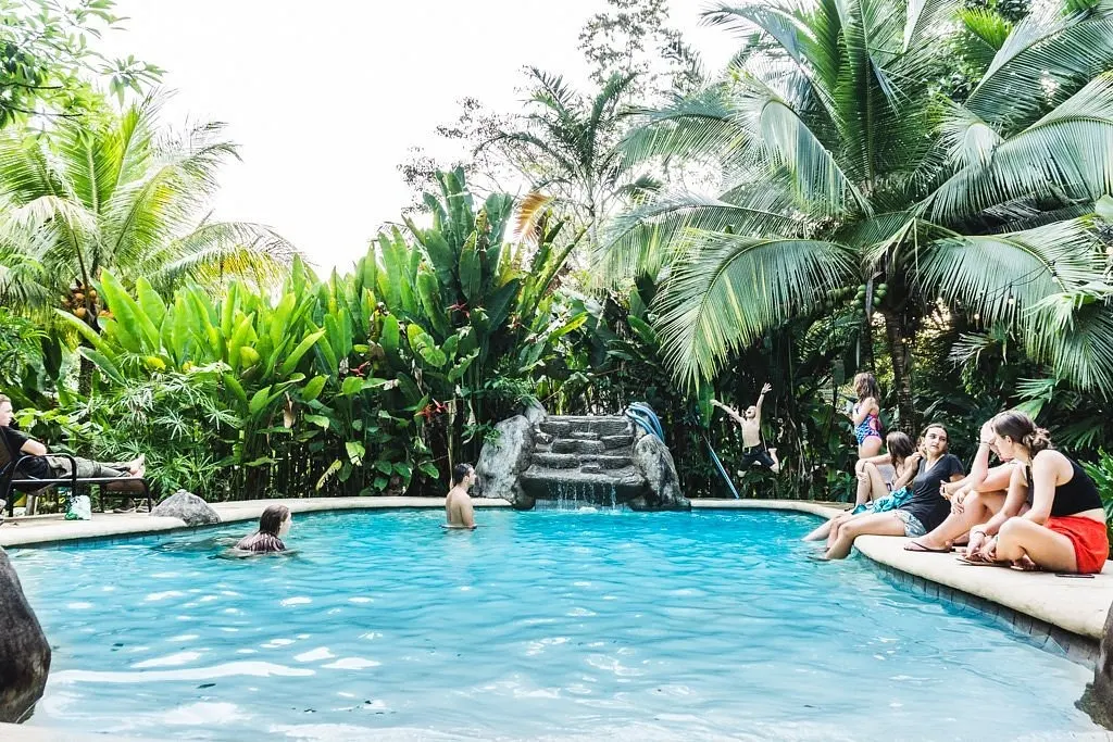 Piscina rodeada de palmeras con huéspedes descansando en el borde